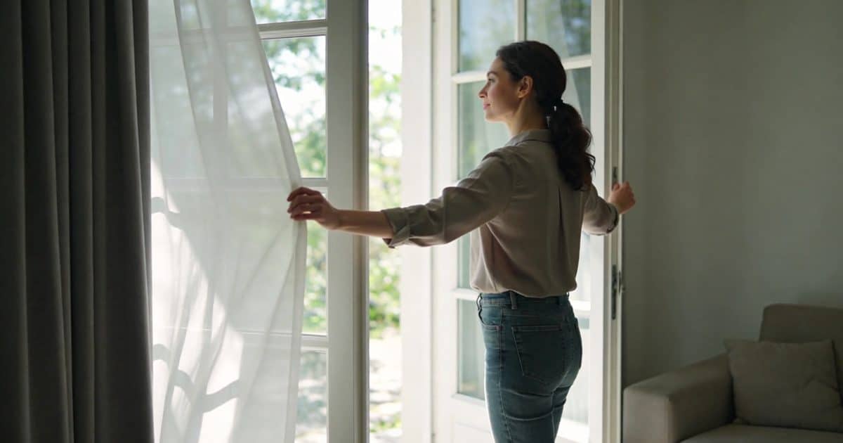 femme ouvrant grand une fenetre ensoleillee aerer salon
