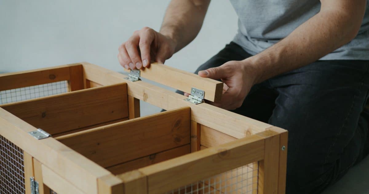 homme agenouille montant un poulailler en bois démontable